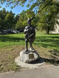 Pomnik postaci w stroju ludowym, stojący na głazie w parku.