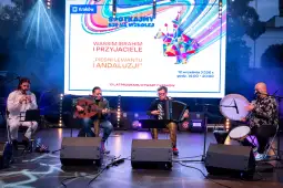 Muzycy grający na instrumentach podczas koncertu w Krakowie. Plakat z informacjami o wydarzeniu.