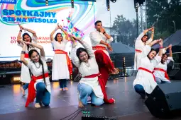 Grupa tancerzy w tradycyjnych strojach wykonuje układ taneczny na scenie.