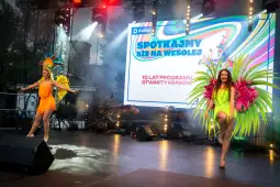 Dwie tancerki w kolorowych strojach z piórami tańczą na scenie podczas wydarzenia w Krakowie.