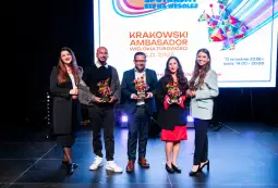 Uczestnicy wydarzenia z nagrodami w rękach, na tle kolorowego tła.