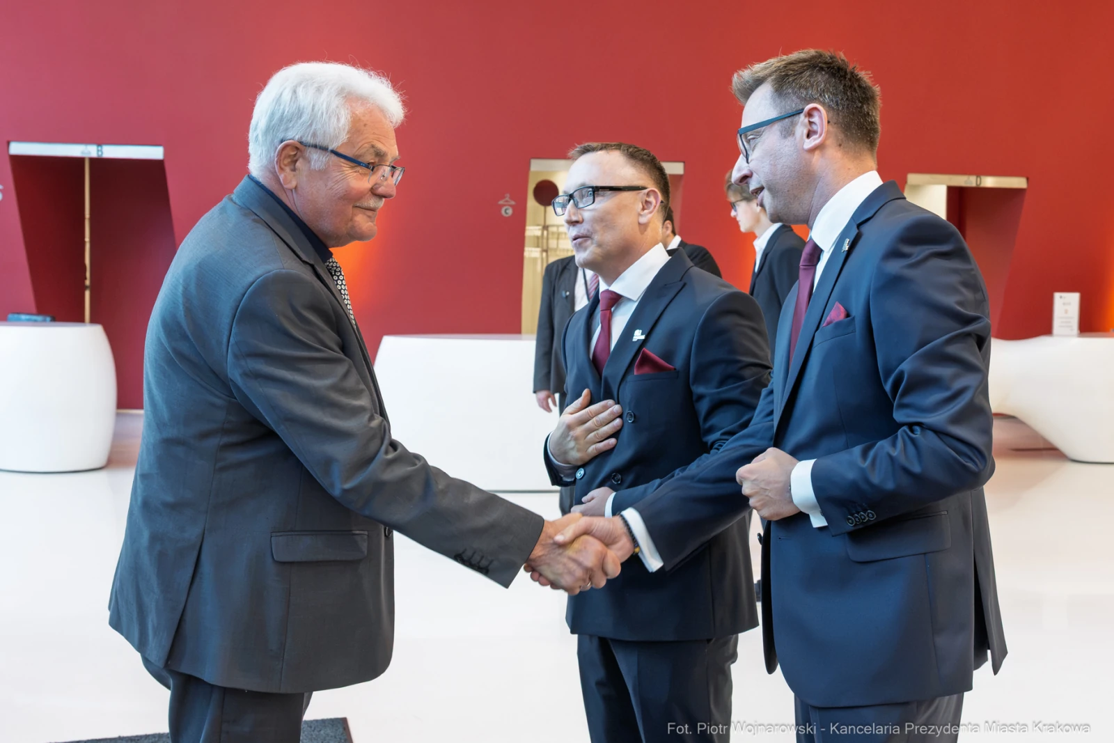 Trzech mężczyzn w garniturach uścisnął sobie dłonie w eleganckim wnętrzu.  Autor: Piotr Wojnarowski