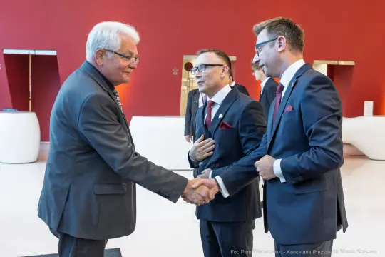 Trzech mężczyzn w garniturach uścisnął sobie dłonie w eleganckim wnętrzu.