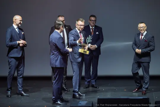 Wręczenie nagrody przez grupę mężczyzn w eleganckich garniturach.