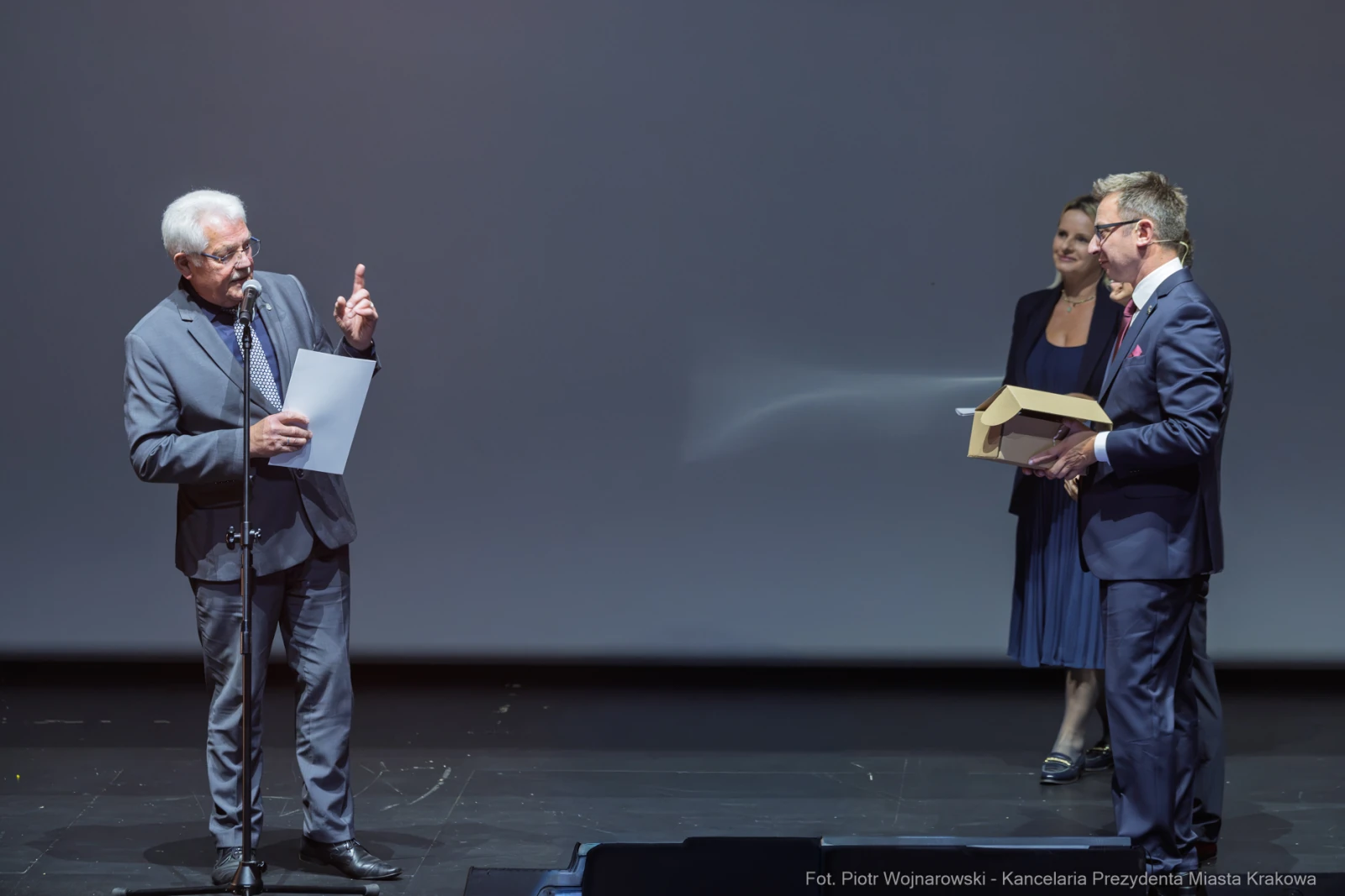 Mężczyzna wręcza nagrodę innemu mężczyźnie na scenie, w tle stoi kobieta.  Autor: Piotr Wojnarowski