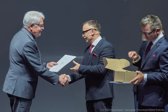 Wręczenie nagrody podczas ceremonii z udziałem trzech mężczyzn w garniturach.