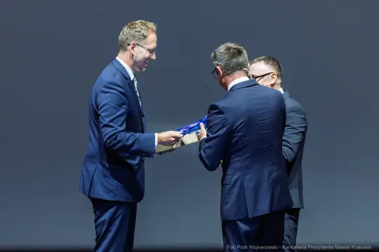 Wręczenie nagrody przez mężczyzn w garniturach na scenie.