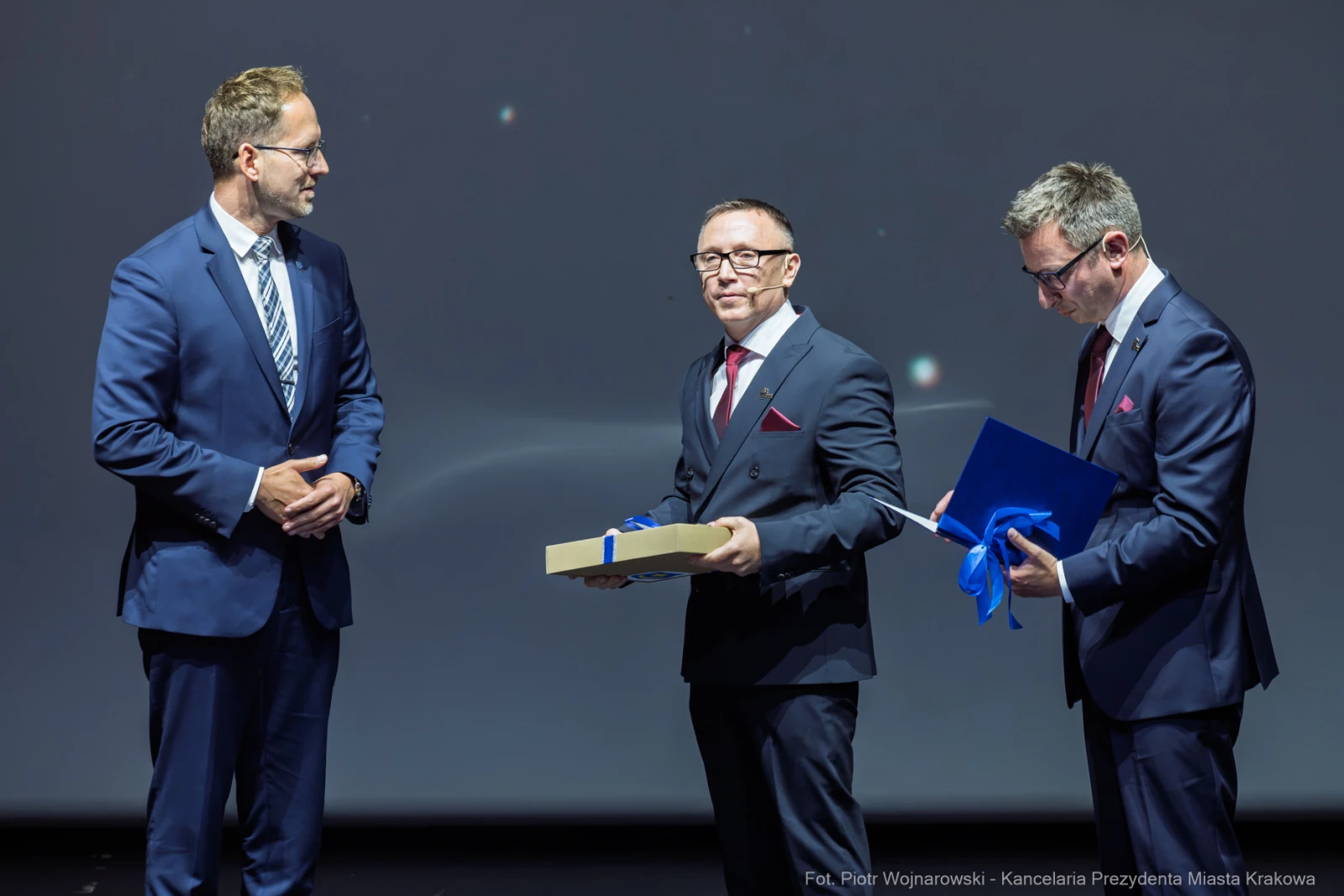Wręczenie nagrody podczas uroczystości z udziałem trzech mężczyzn w garniturach.  Autor: Piotr Wojnarowski