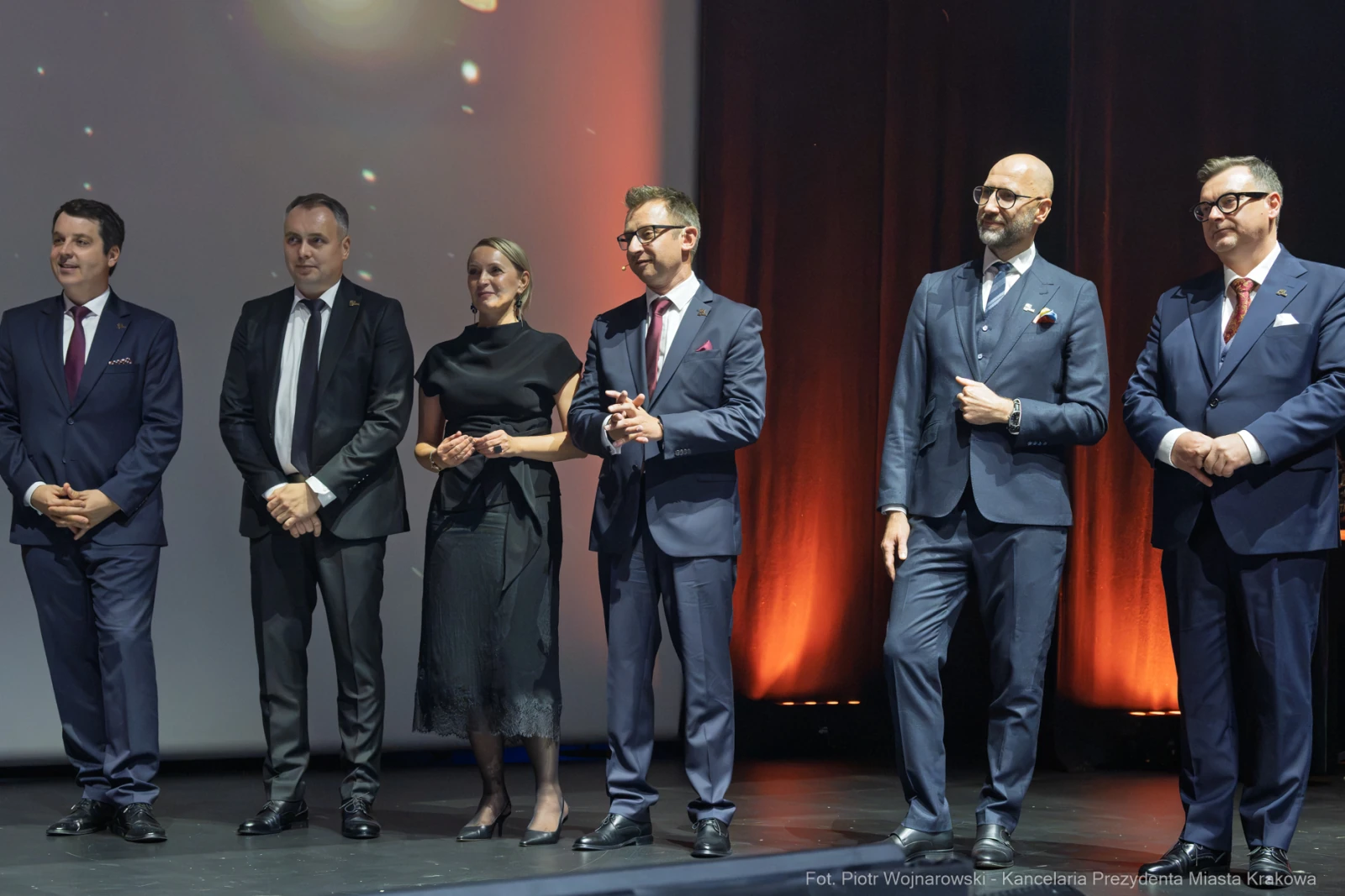 Grupa elegancko ubranych mężczyzn i kobieta na scenie podczas wydarzenia.  Autor: Piotr Wojnarowski