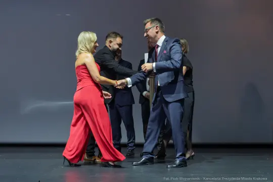 Uroczystość wręczenia nagrody, uściski dłoni, eleganckie stroje.