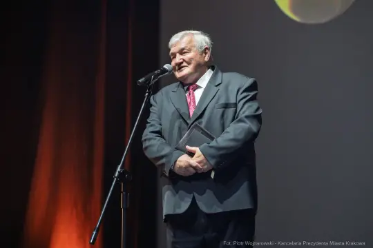 Mężczyzna w garniturze przemawia do publiczności z mikrofonem w ręku.