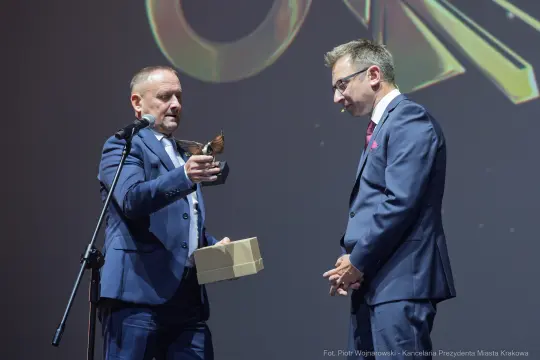 Mężczyzna wręcza nagrodę innemu mężczyźnie na scenie podczas uroczystości.