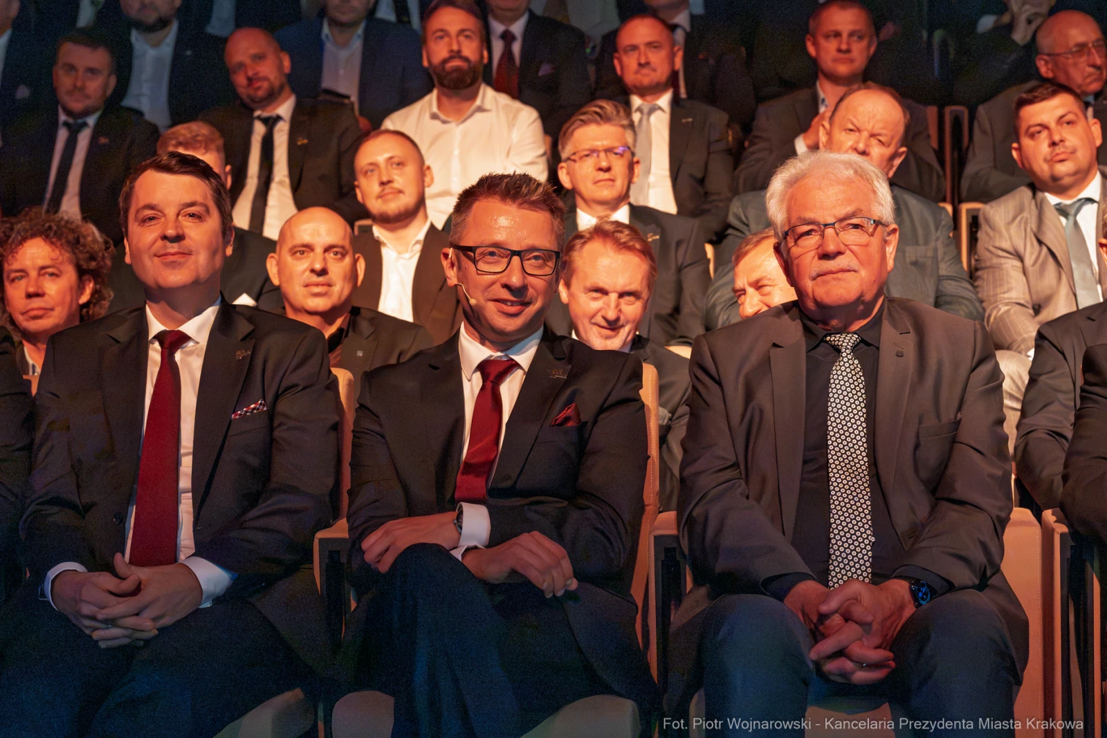 Grupa mężczyzn w garniturach siedzących na widowni, uśmiechających się i rozmawiających.  Autor: Piotr Wojnarowski