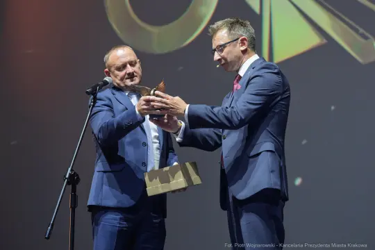 Wręczenie nagrody przez mężczyznę w garniturze drugiemu mężczyźnie z trofeum w ręku.