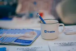 Kubek z logo Krakowa, długopis i ulotki na stole.