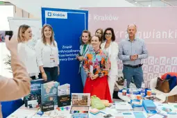 Grupa ludzi przy stoisku promującym Kraków, z materiałami informacyjnymi i gadżetami.