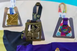 Medale sportowe na stojakach, różne kolory i kształty, obok koszulki.