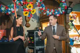 Kobieta i mężczyzna na scenie, prowadzą rozmowę, w tle dekoracje kwiatowe.
