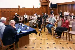 Konferencja prasowa z dziennikarzami i kamerzystami w sali z drewnianymi panelami.