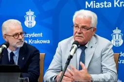 Dwóch mężczyzn podczas konferencji prasowej, jeden mówi do mikrofonu. Tło z logo miasta Krakowa.