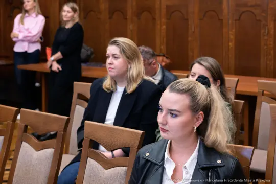 Grupa osób siedzących w sali, skupionych na wydarzeniu.