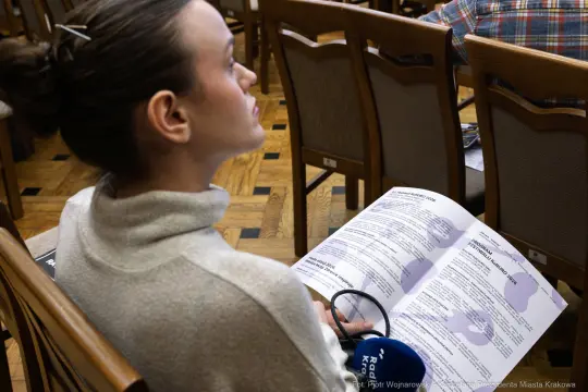 Kobieta siedząca na spotkaniu, trzymająca dokumenty i mikrofon.