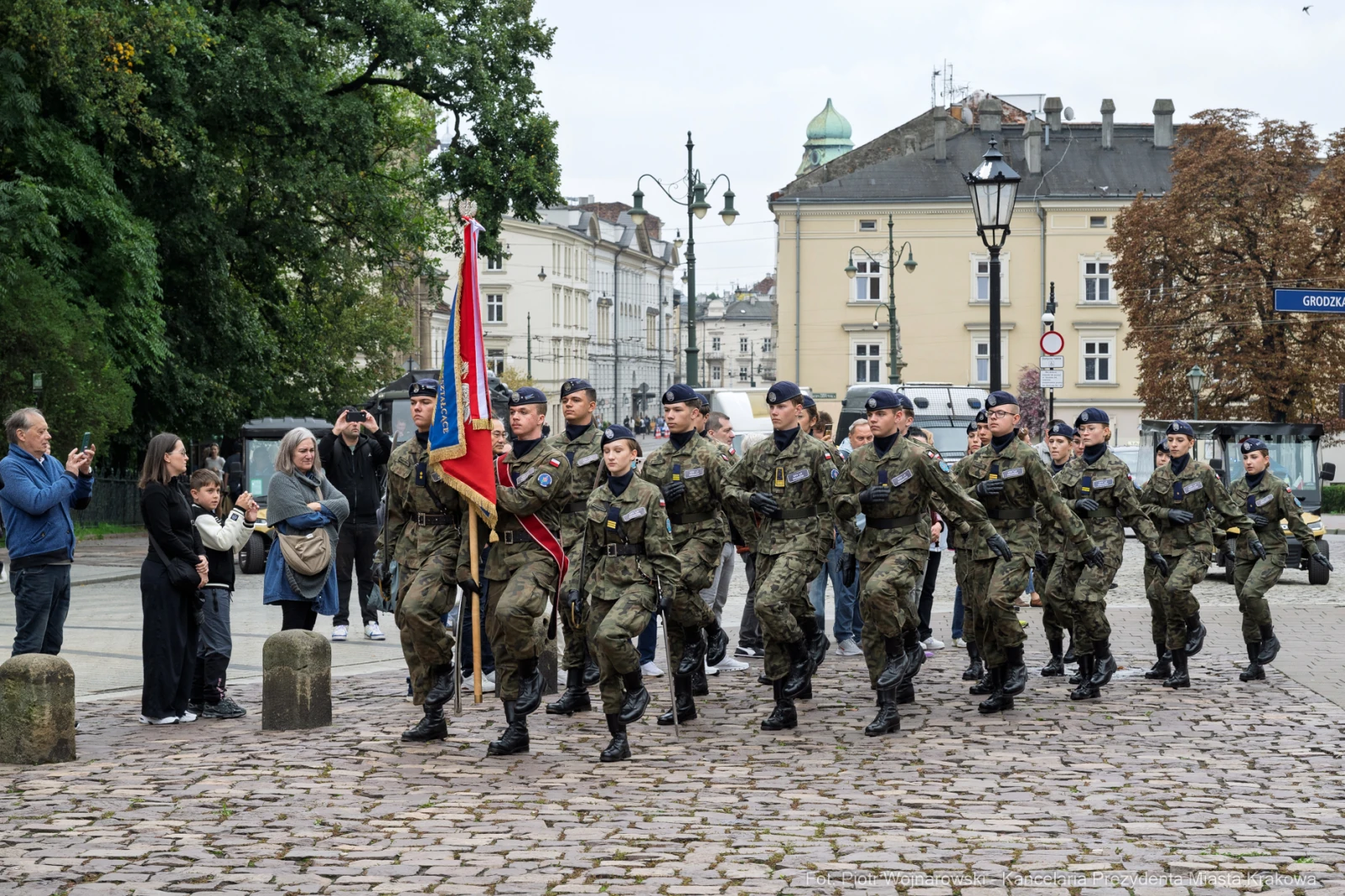 Żołnierze w mundurach maszerują z flagą, obok obserwatorzy na ulicy.  Autor: Piotr Wojnarowski