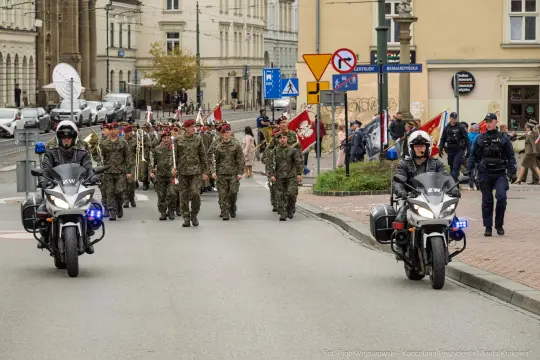 Marsz żołnierzy z flagami, eskortowany przez policję na ulicy.