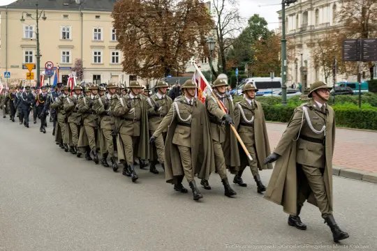 Żołnierze w mundurach maszerujący w kolumnie z flagami.