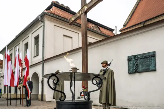 Pomnik upamiętniający ofiary Katynia z wartownikami i zniczem. Flagi Polski w tle.
