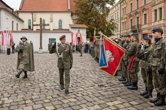 Uroczystość wojskowa z flagami i żołnierzami w mundurach.