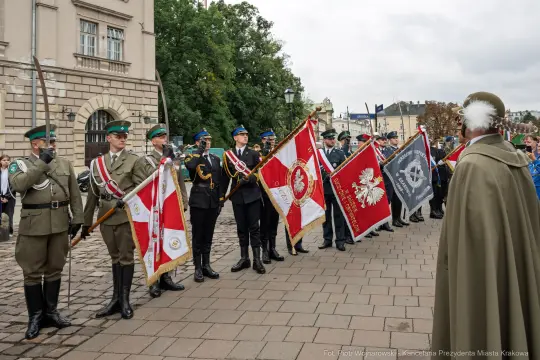 Uroczystość z udziałem żołnierzy i sztandarów w historycznym otoczeniu.