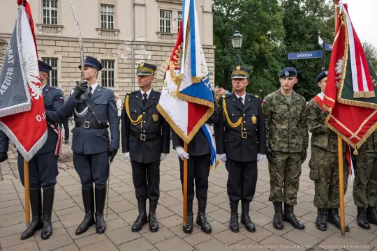 Grupa mężczyzn w mundurach, trzymających sztandary, podczas uroczystości.