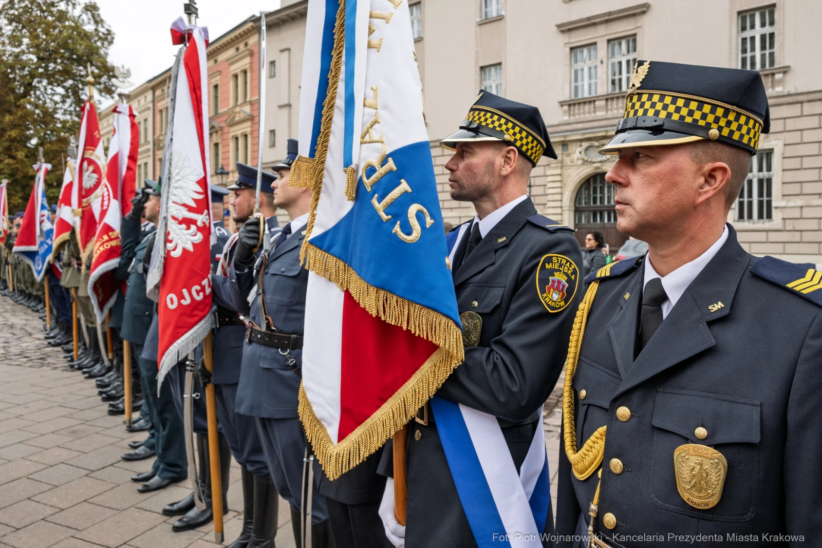 Uroczystość z udziałem strażników miejskich i flag, w tle historyczna architektura.  Autor: Piotr Wojnarowski