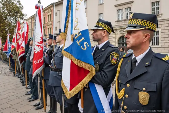 Uroczystość z udziałem strażników miejskich i flag, w tle historyczna architektura.