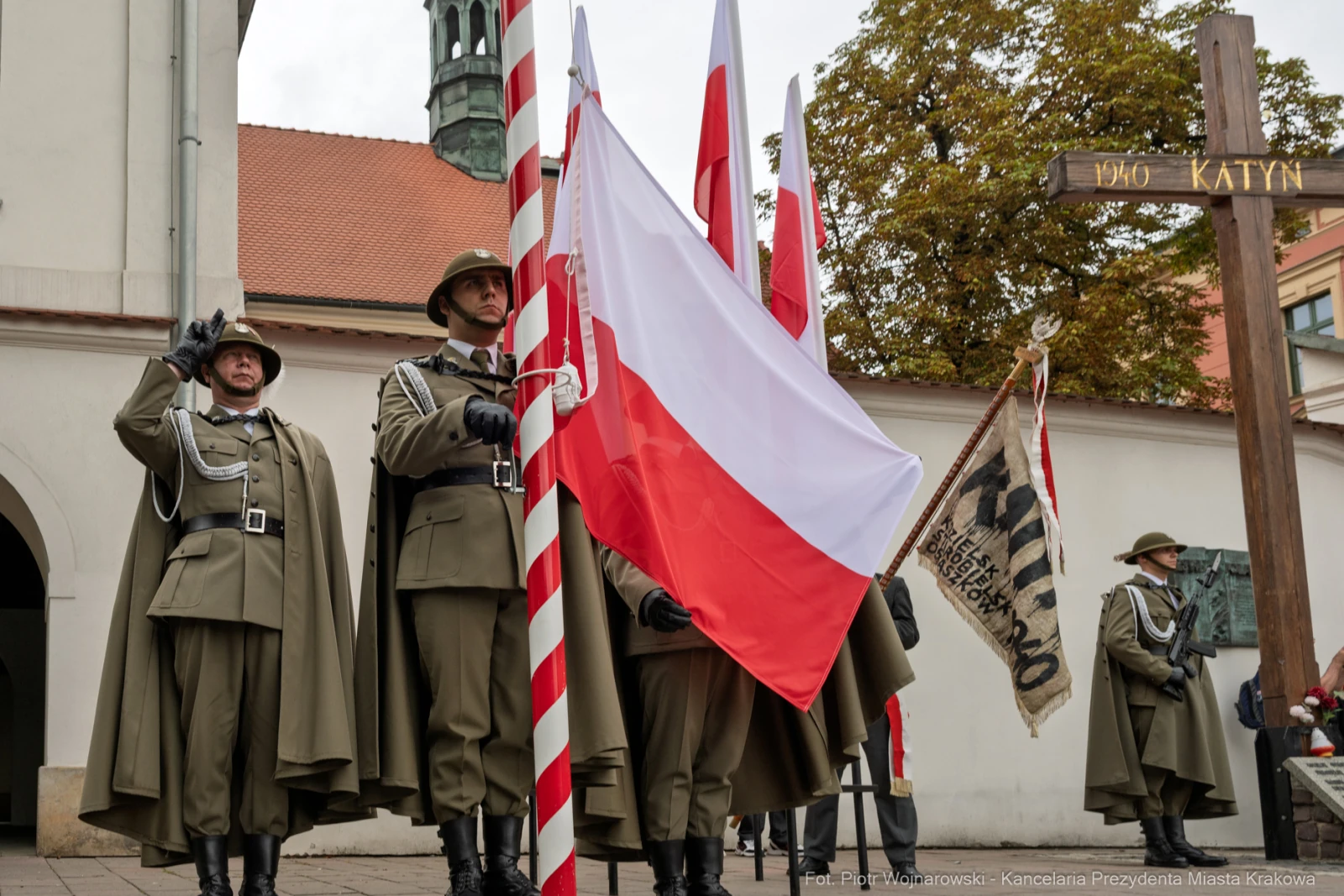 Żołnierze w mundurach trzymają flagę Polski i sztandar, obok krzyż upamiętniający Katyń.  Autor: Piotr Wojnarowski