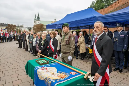 Ceremonia z udziałem żołnierzy, flagi i uczestników w strojach galowych.