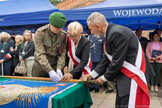 Uroczystość z udziałem wojskowych i przedstawicieli władz, składanie hołdu na tle flagi.