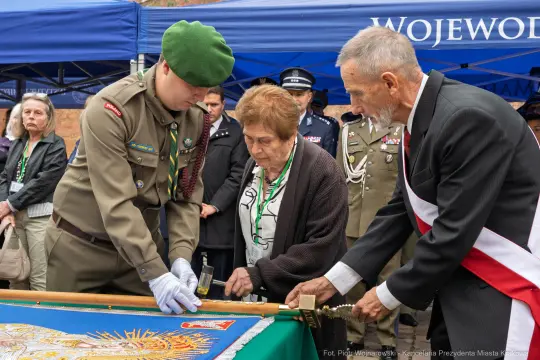 Ceremonia składania kwiatów przy sztandarze, uczestnicy w mundurach i odznaczeniach.