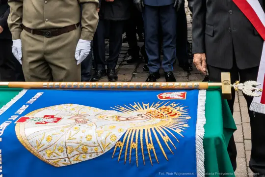 Sztandar z wizerunkiem Matki Boskiej i herbem, trzymany przez żołnierzy podczas ceremonii.