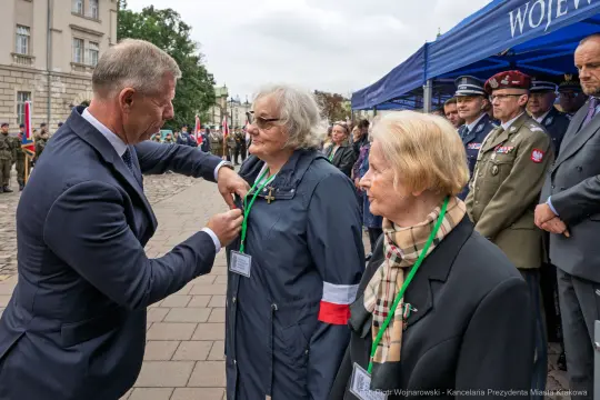 Uroczystość wręczenia odznaczeń dwóm kobietom w mundurach, w obecności oficjeli.
