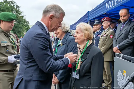 Wręczenie odznaczenia przez mężczyznę starszej kobiecie podczas ceremonii.