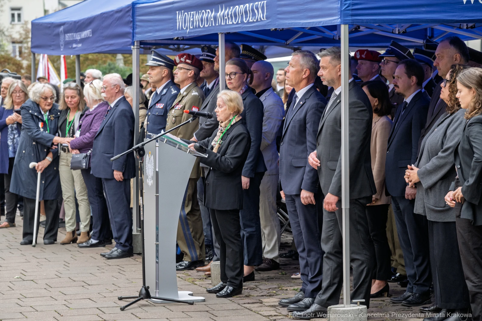 Uroczystość z przemówieniem, uczestnicy w mundurach i garniturach, flagi Polski.  Autor: Piotr Wojnarowski