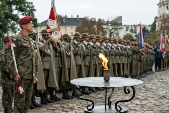 Ceremonia wojskowa z żołnierzami w mundurach i płonącym zniczem.