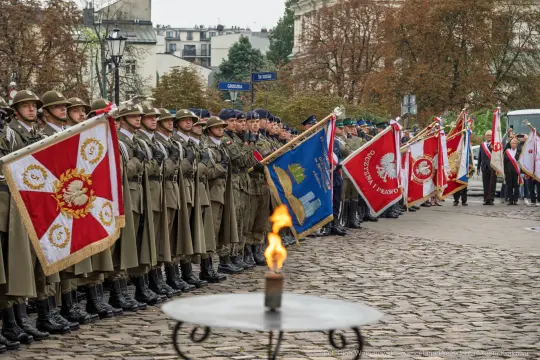 Uroczystość z udziałem żołnierzy w mundurach, sztandarów i znicza w tle.