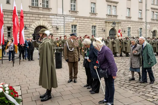 Uroczystość z udziałem żołnierzy i osób cywilnych, z flagami Polski i zniczami.