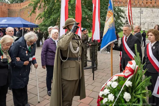 Uroczystość patriotyczna z udziałem żołnierzy, flagi i kwiatów.