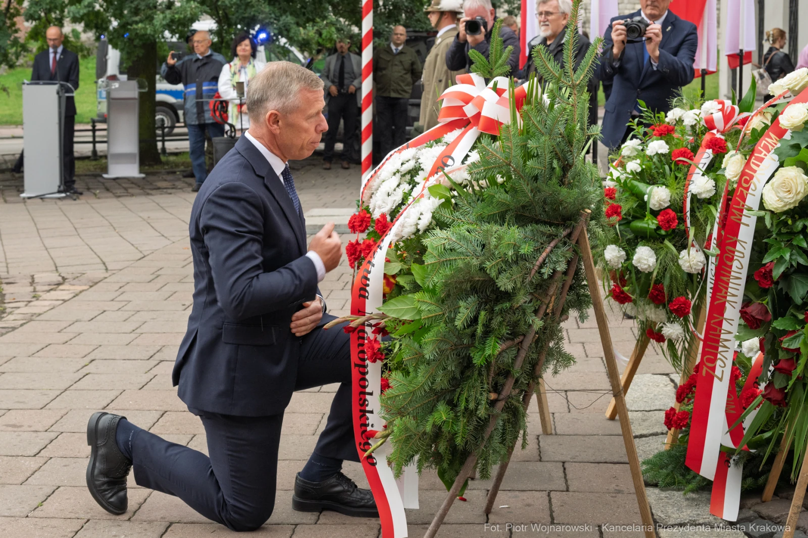 Mężczyzna klęczy przy wieńcu z kwiatów, składając hołd.  Autor: Piotr Wojnarowski