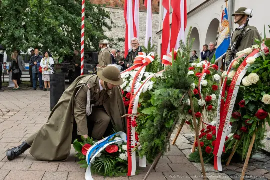 Żołnierz składa wieniec z kwiatów w otoczeniu flag narodowych.