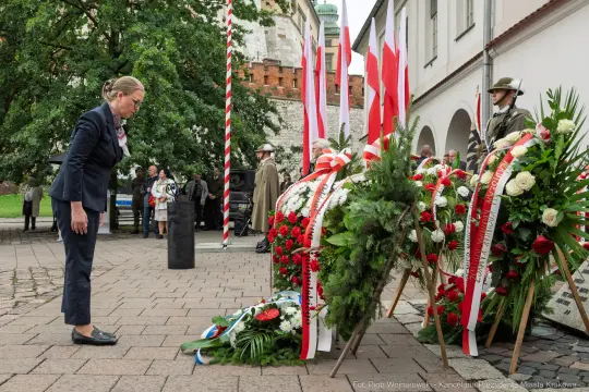 Kobieta składa hołd przy wieńcach z kwiatów i flagami narodowymi.
